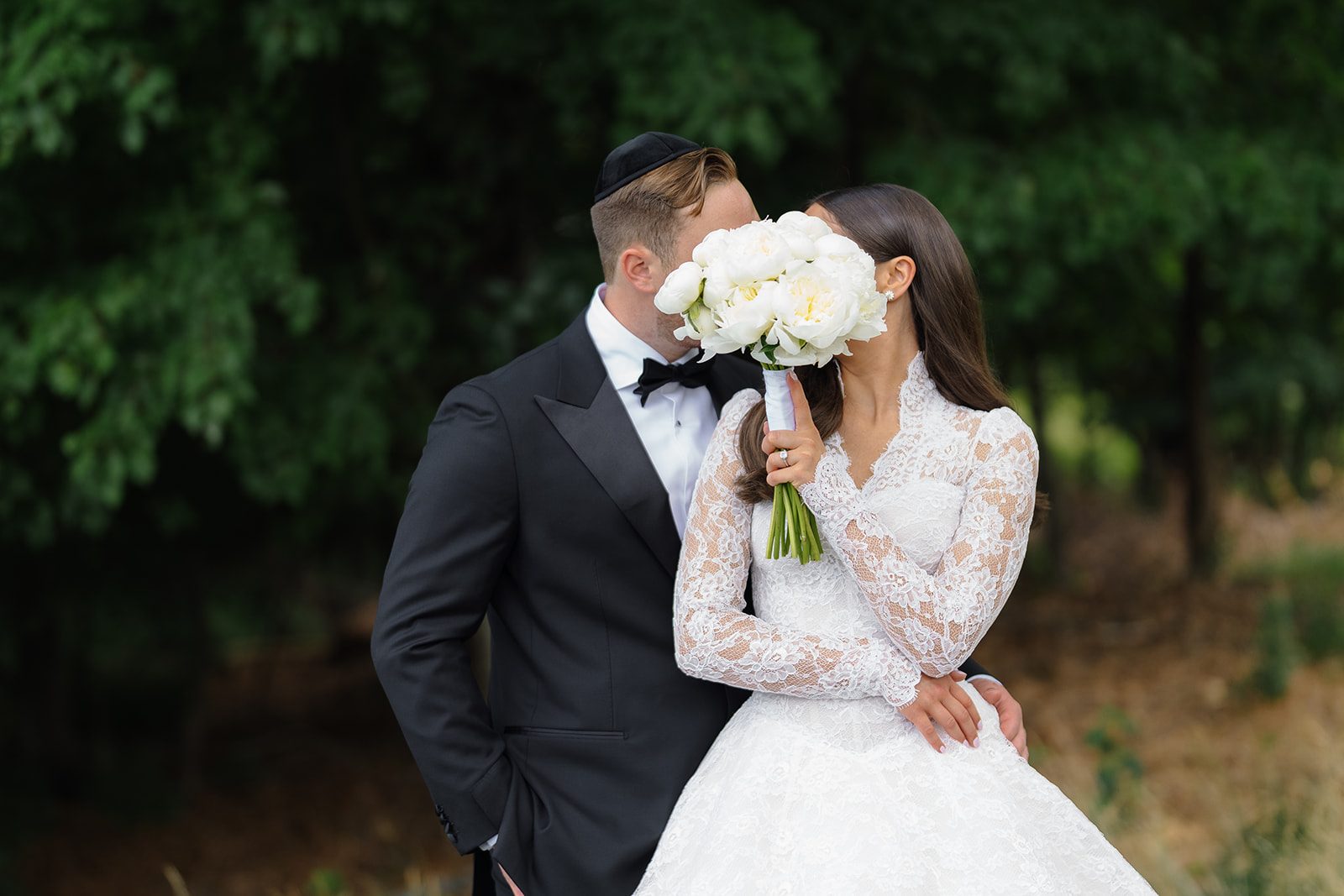 Groom kissing bride behind her white peony bouquet at Edgewood Country Club