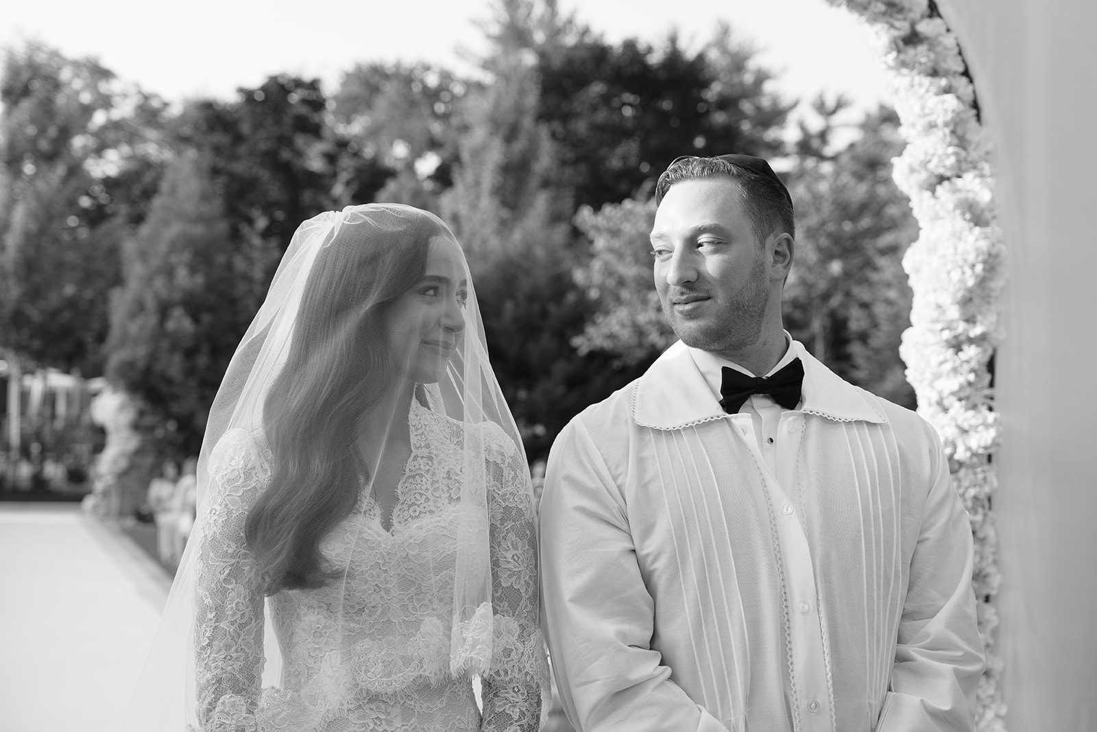Black and white portrait of the couple under the chuppah, bride veiled