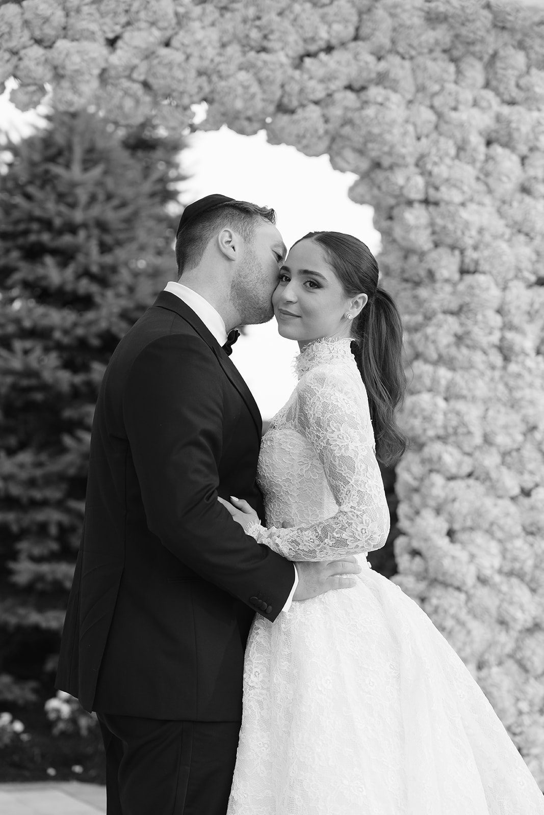 Black and white kiss beneath the white floral arch at Edgewood Country Club