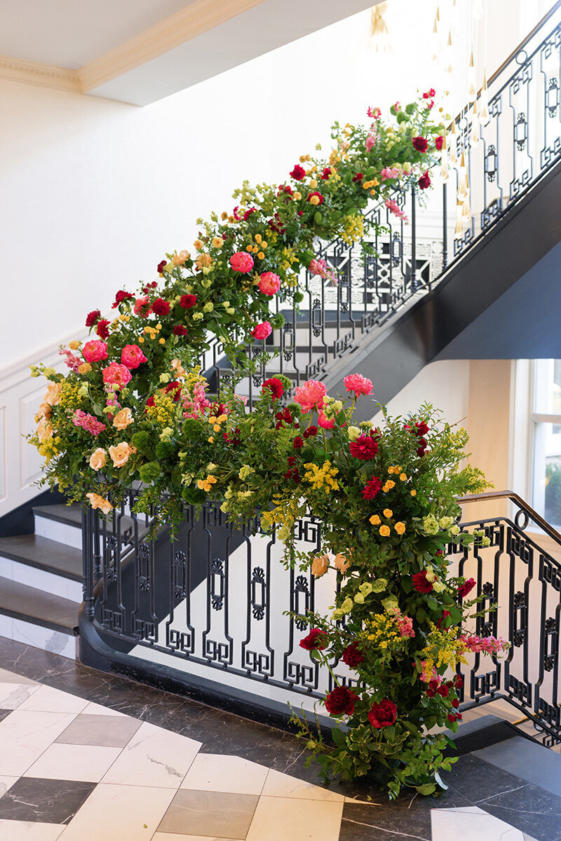 The Lannin's black iron staircase wrapped in garlands of red, pink, and yellow flowers.