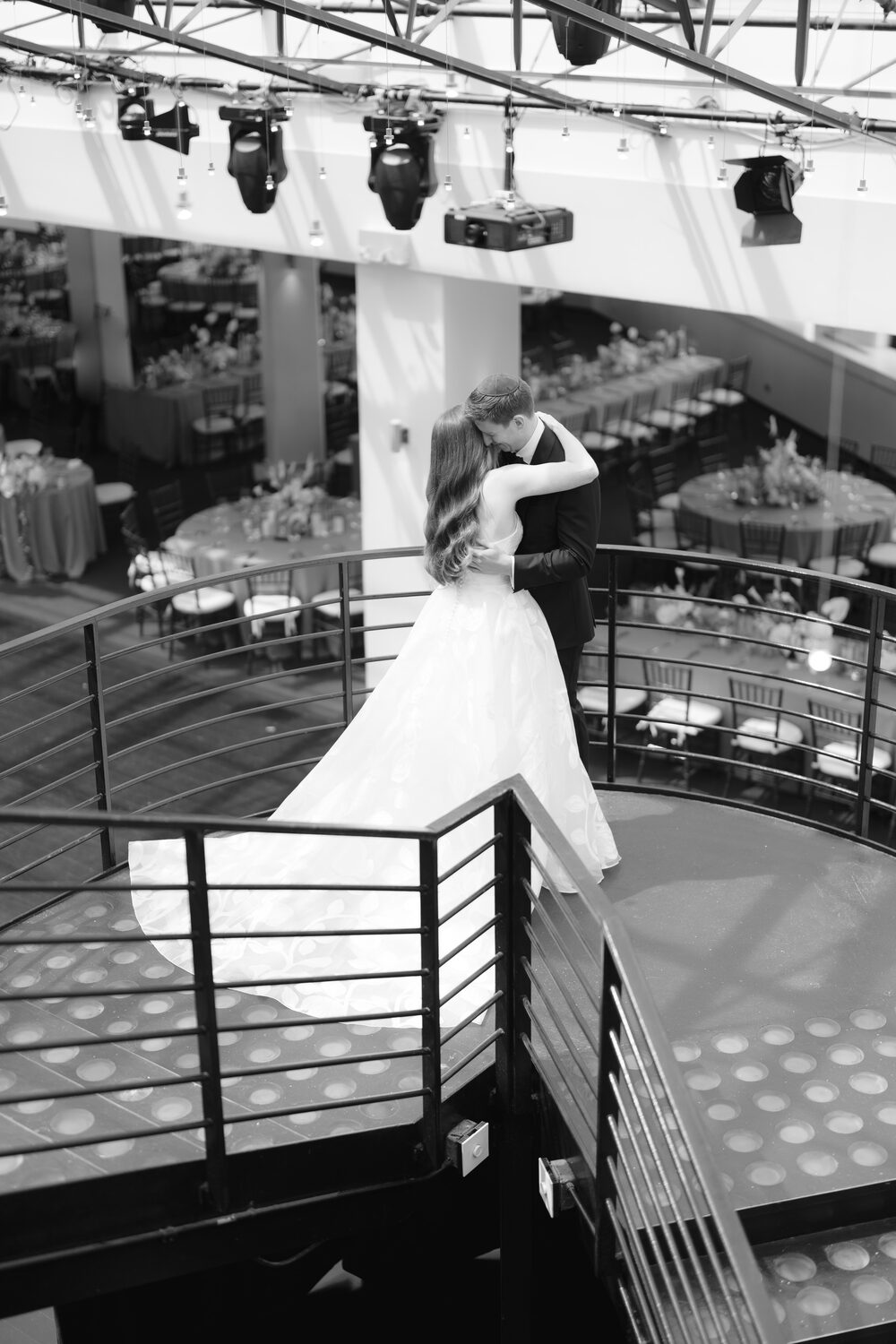 The bride raises an arm at the balcony railing in black and white.