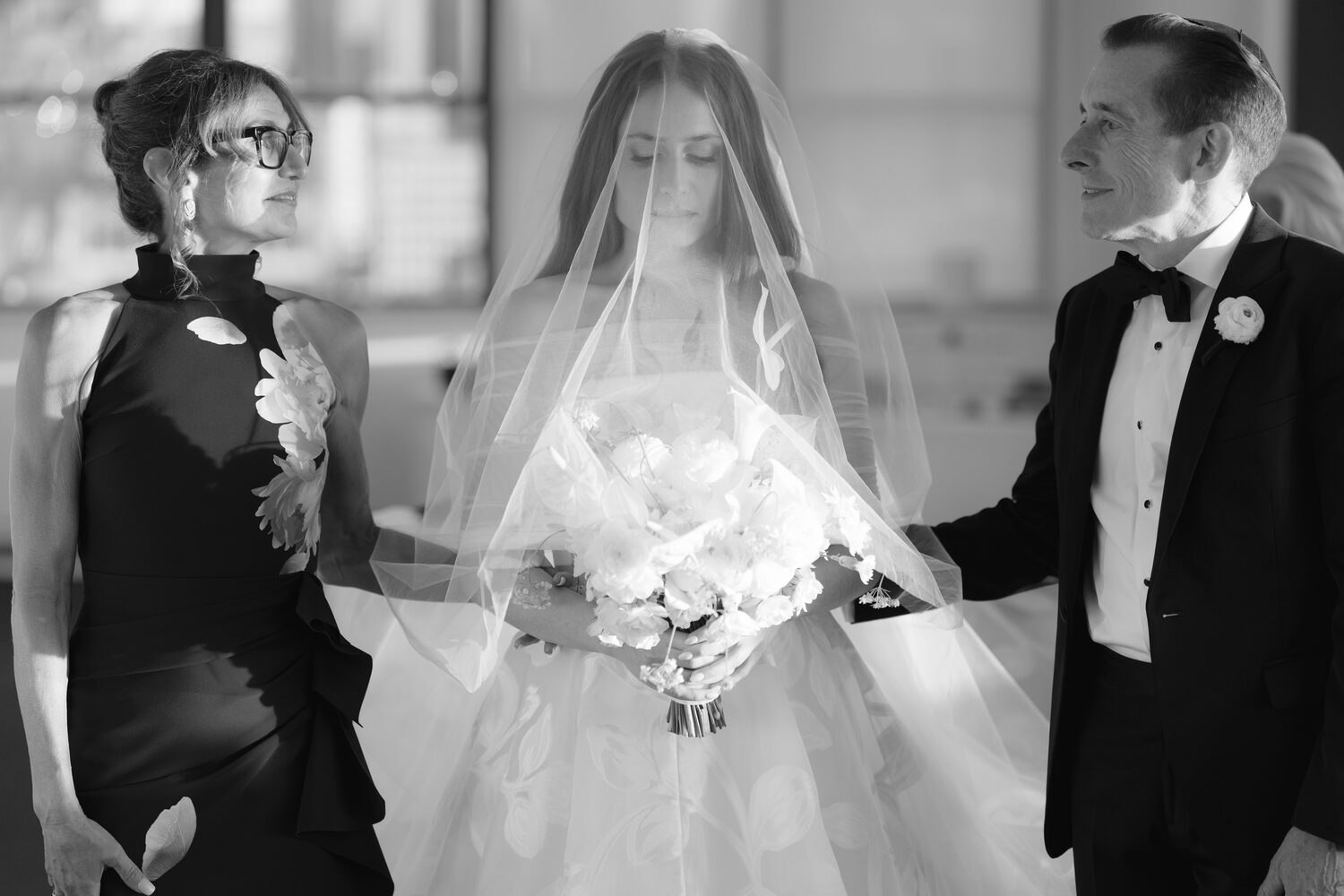 A black and white moment as the bride walks between her mother and father.