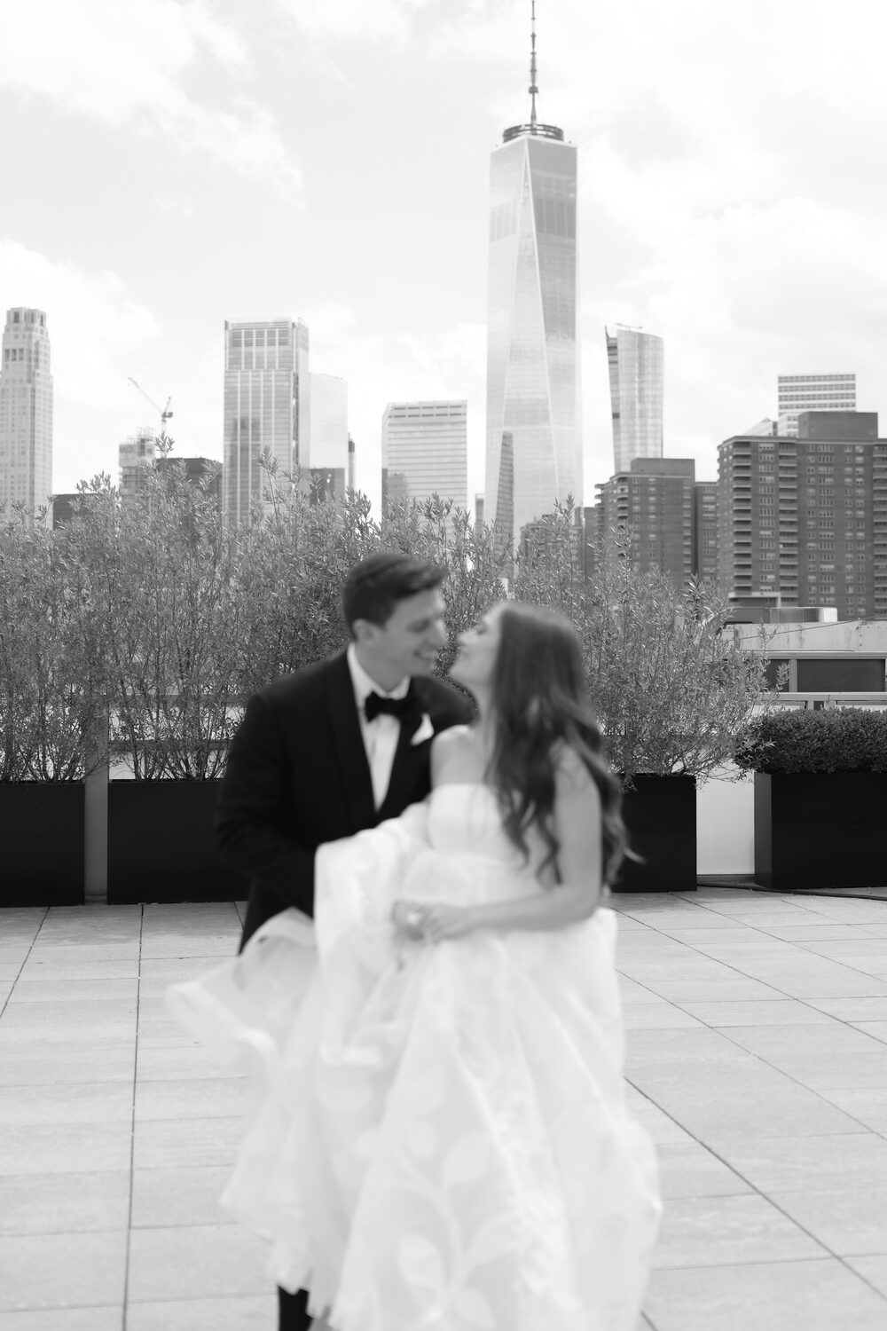 A black and white frame of the couple walking the rooftop with One World Trade Center in view.