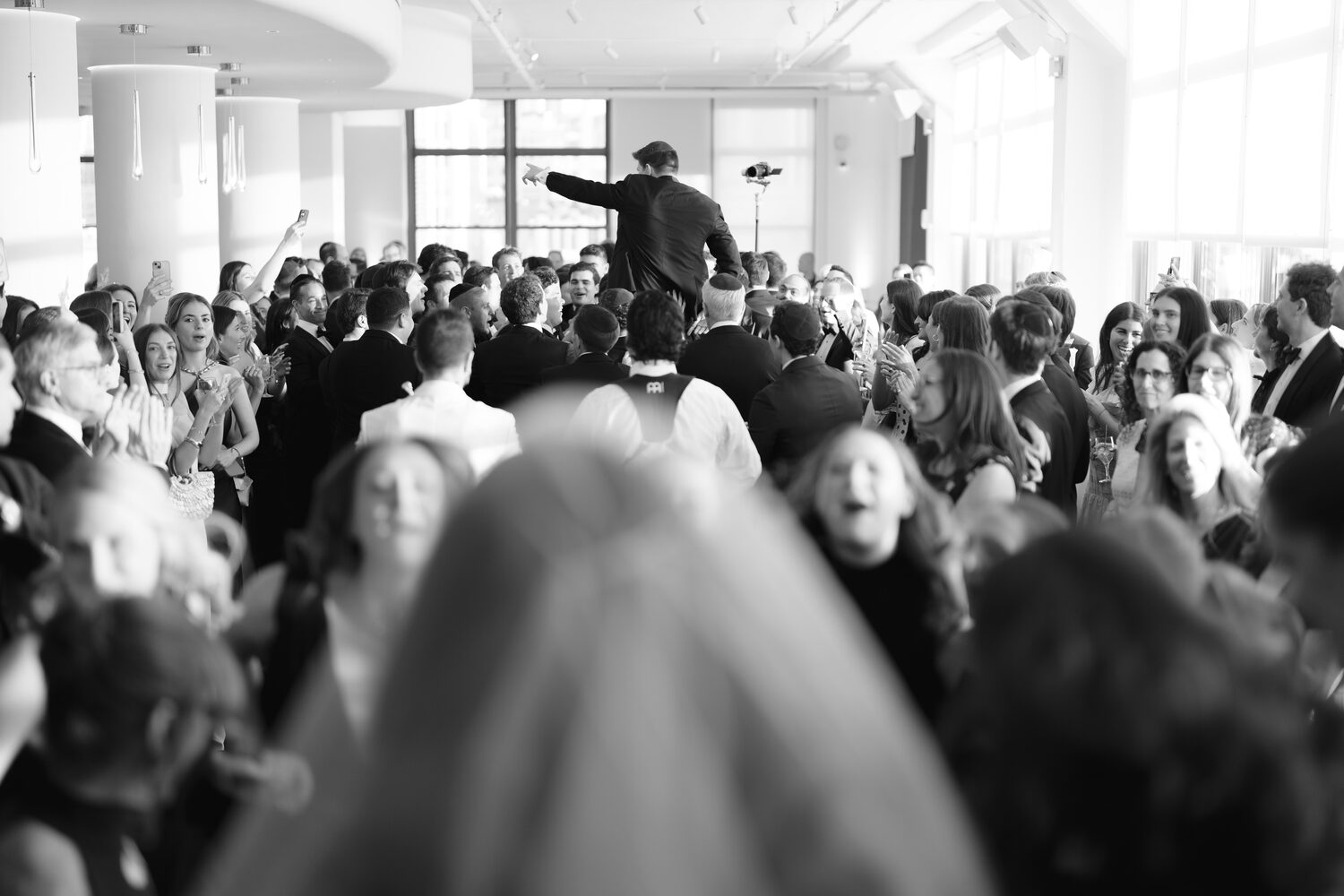 A black and white frame of the bride's veil in the crowd as the bandleader calls the room.