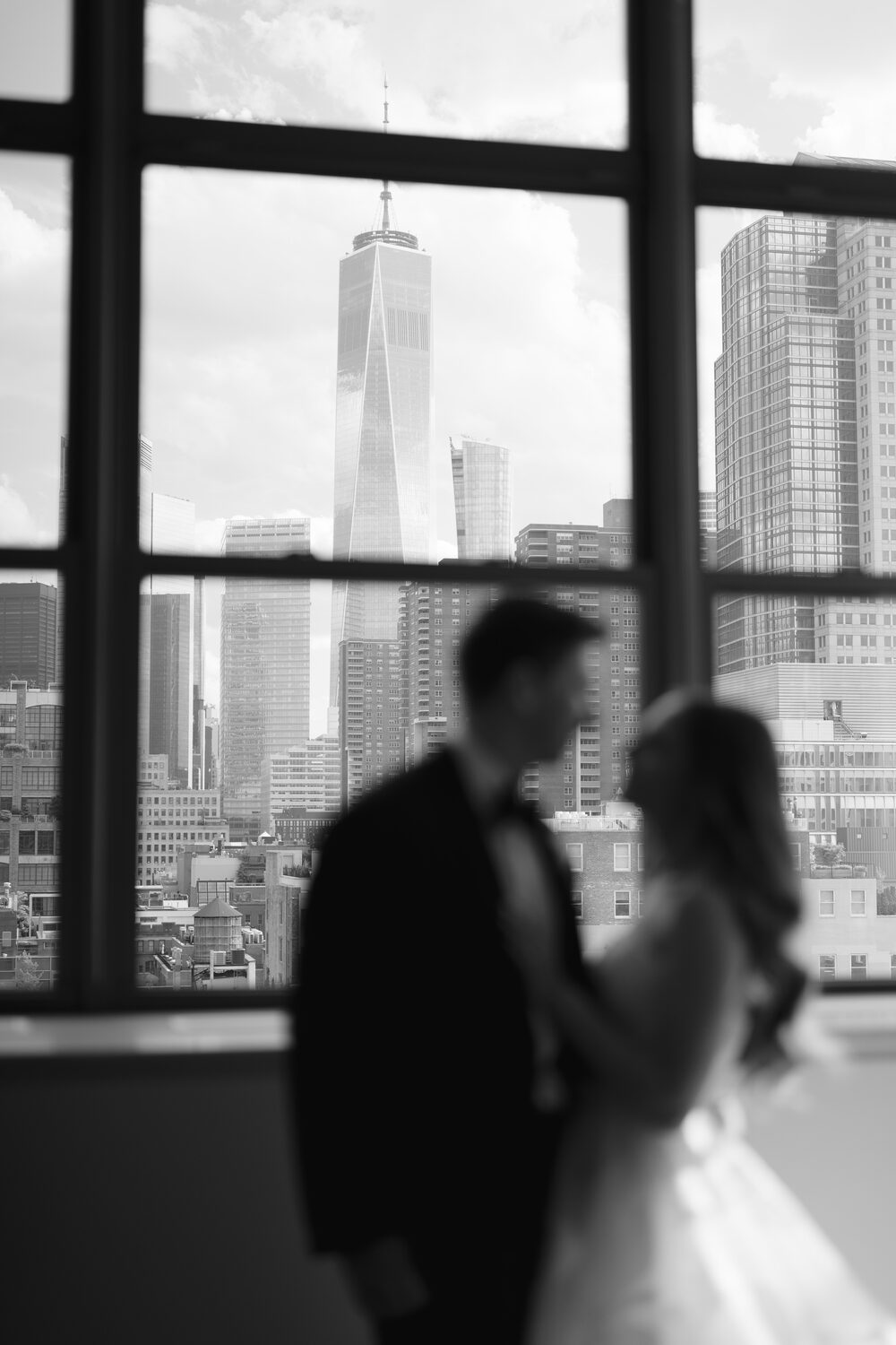 Silhouetted against a downtown window in black and white, the couple leans together.