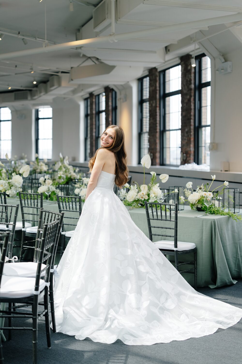 The bride stands alone in the empty ceremony room, her train sweeping across the floor.
