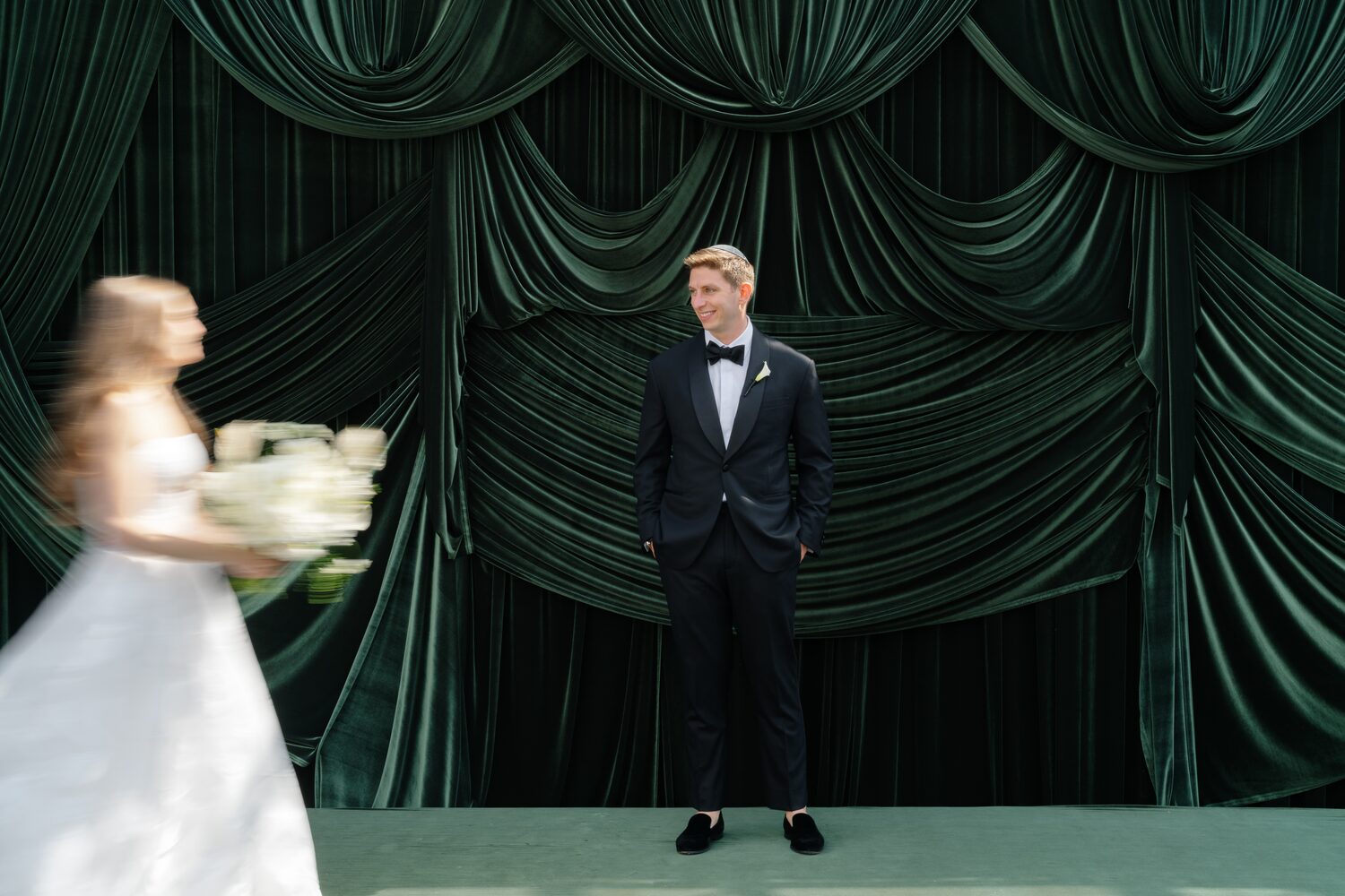 The bride moves toward her groom in a blur of motion against the emerald drapery.