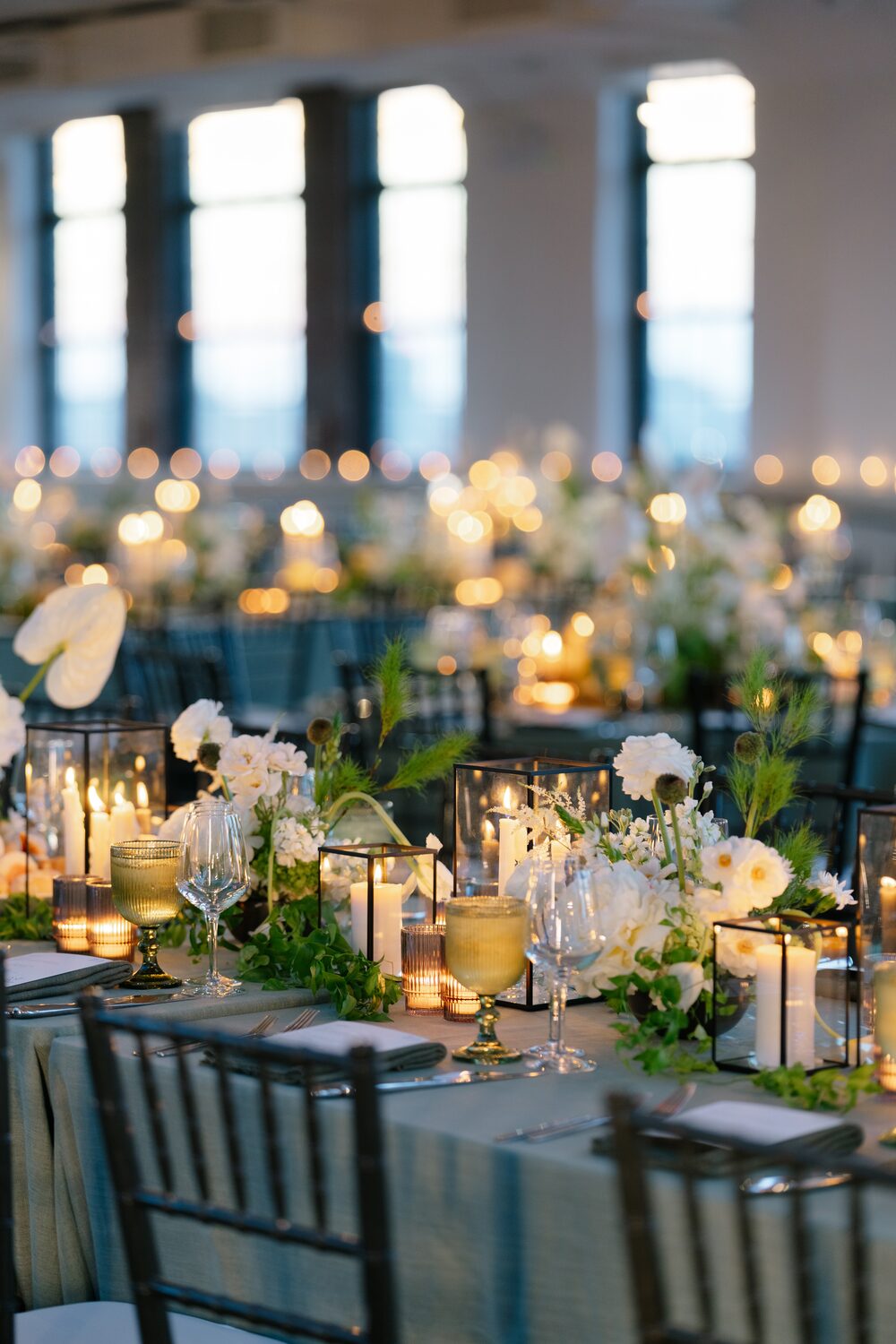 Candlelight and white blooms across a reception table dressed in sage linens.