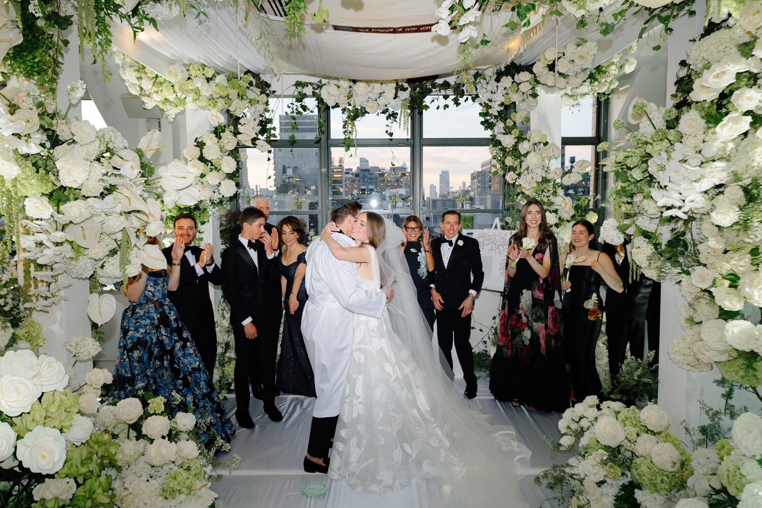 Guests cheer around the couple under the chuppah as the ceremony ends.
