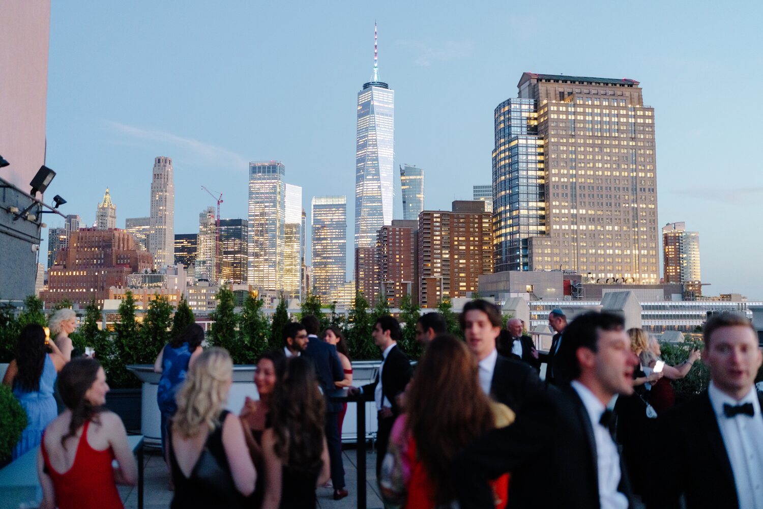 Guests mingle on the rooftop at dusk as the downtown skyline lights up.
