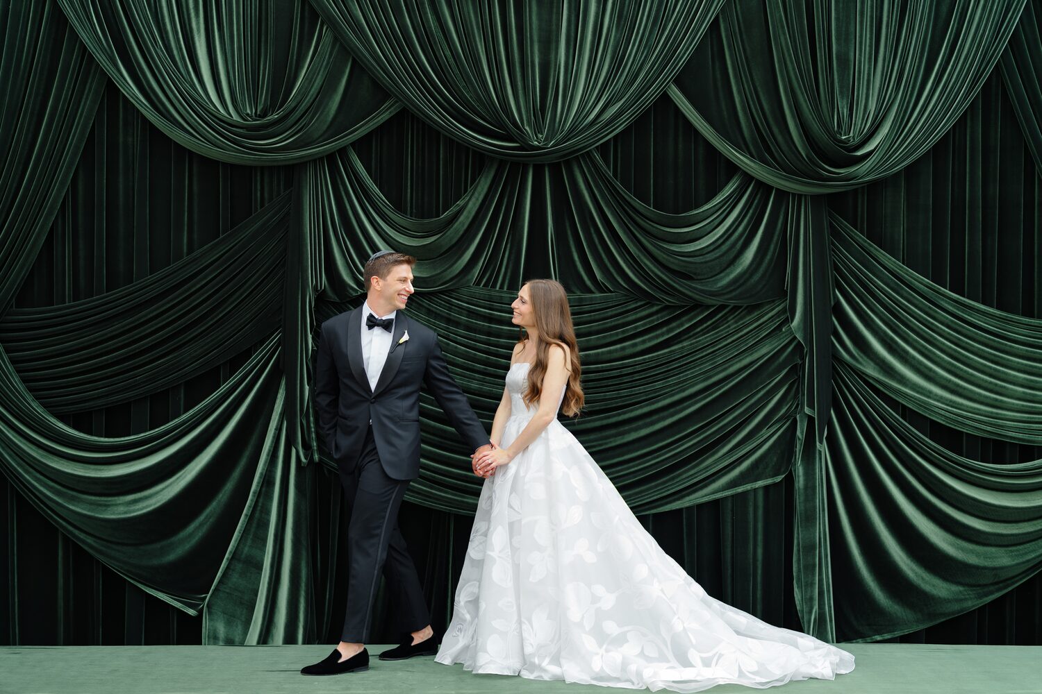 Bride and groom stand apart on the velvet stage, looking at one another.