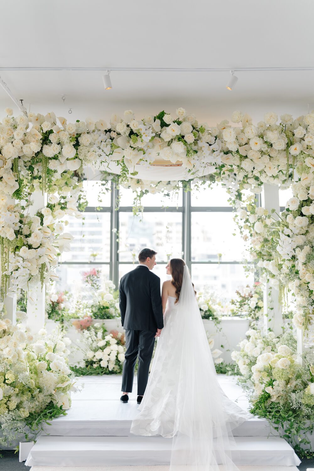 The newlyweds walk away down the white aisle beneath the floral arch.