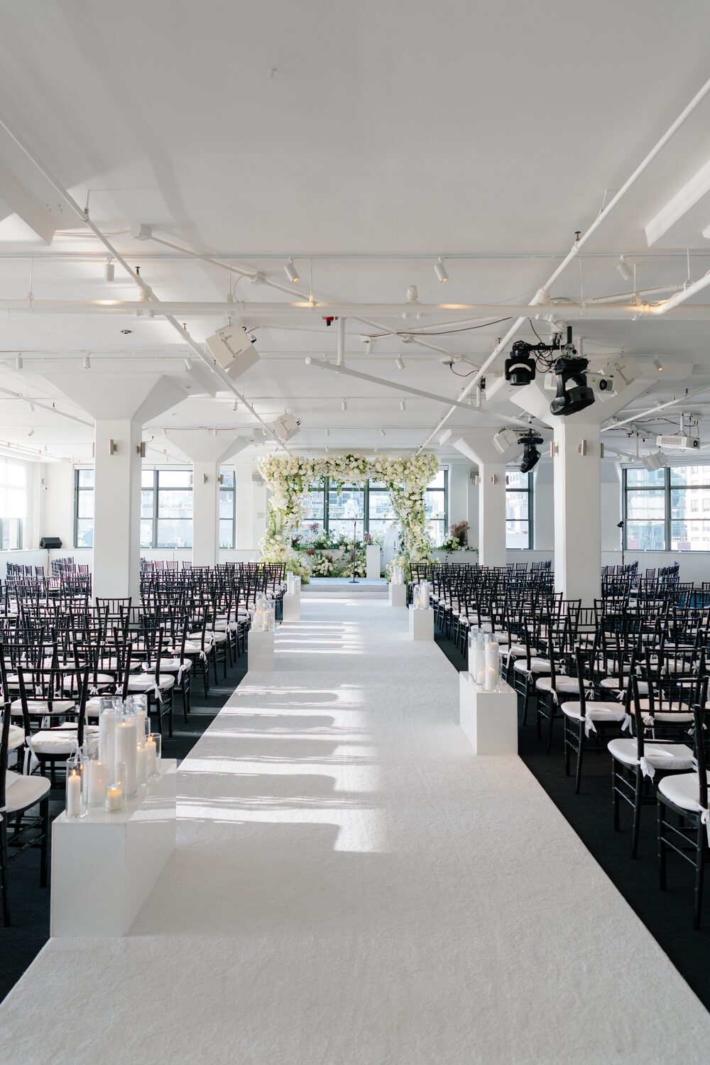 The empty ceremony aisle, white runner and black chairs leading toward the chuppah.