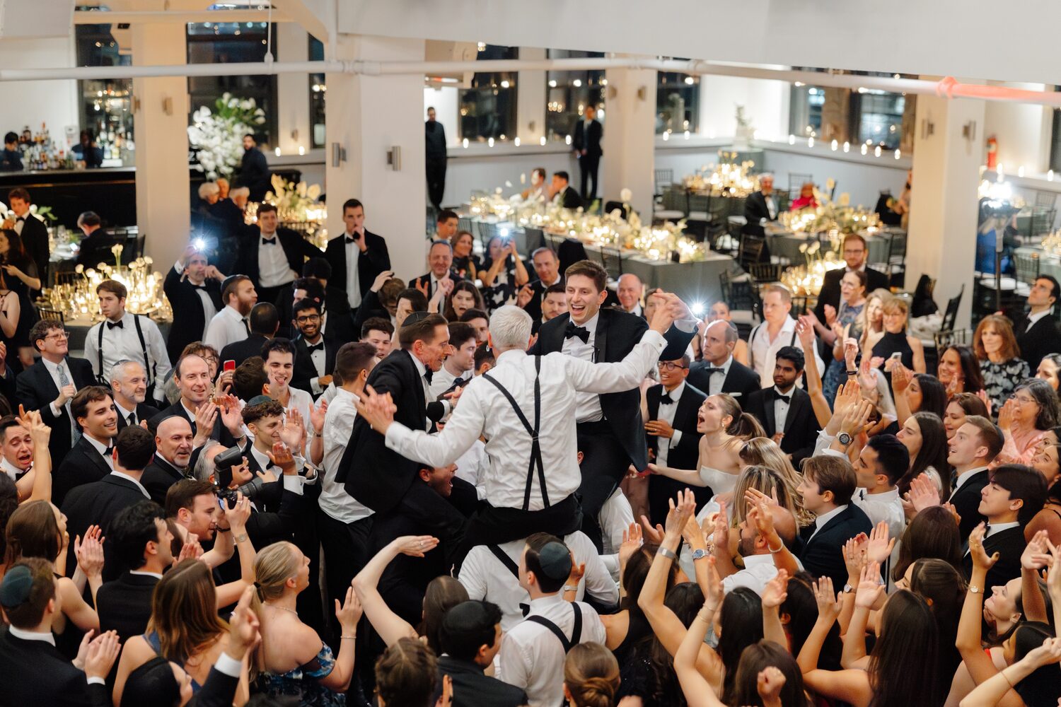 The groom in his kittel is swallowed by a celebrating crowd on the dance floor.