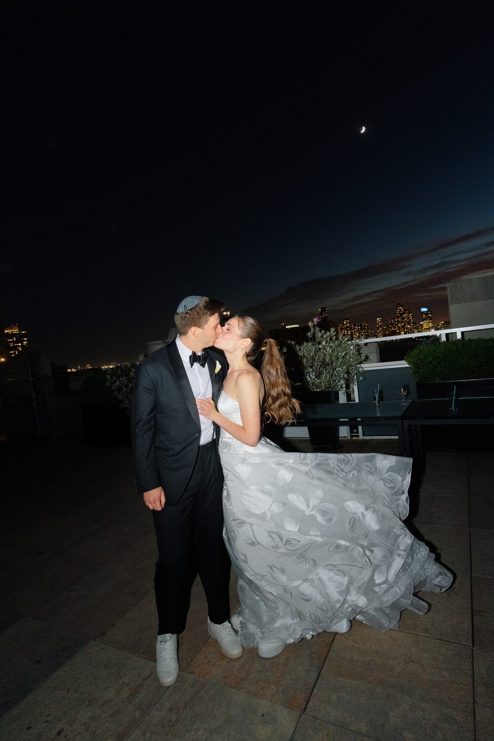A kiss on the rooftop after dark, the Manhattan night behind them.