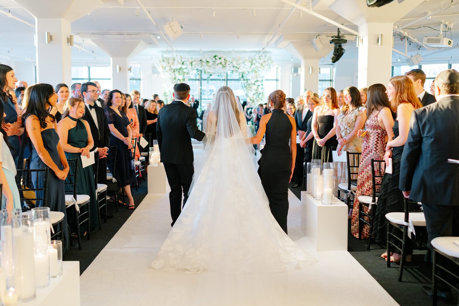 The bride's cathedral train trails behind her as she is walked down the aisle.