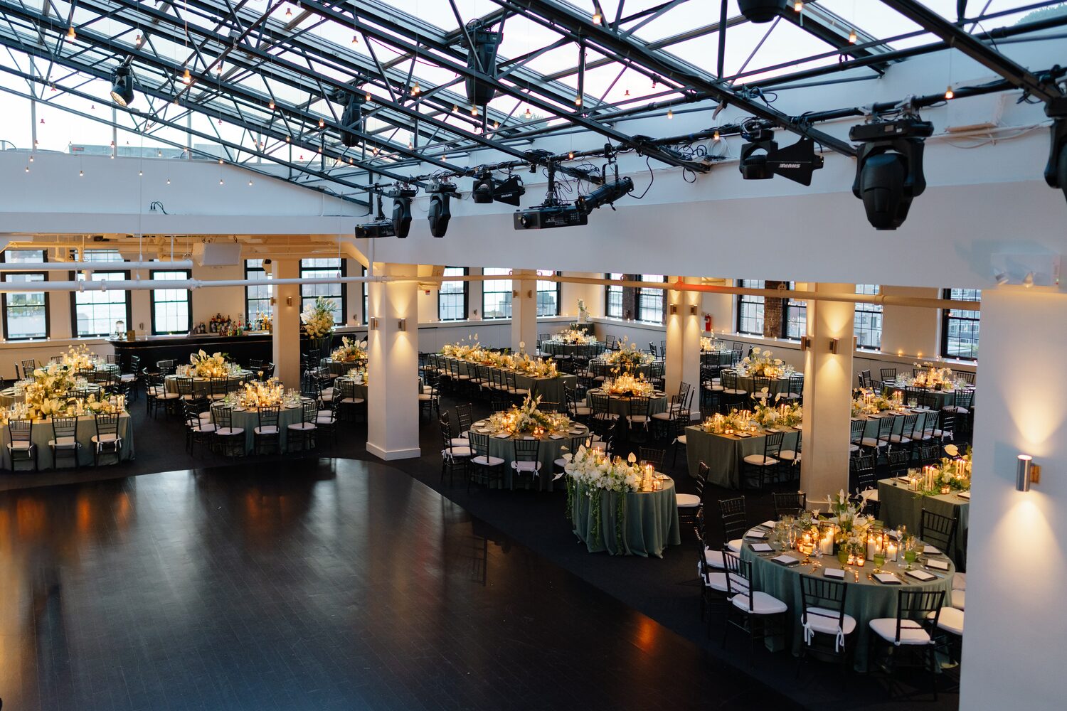 The reception room glows amber beneath Tribeca Rooftop's glass roof, tables set for 292 guests.