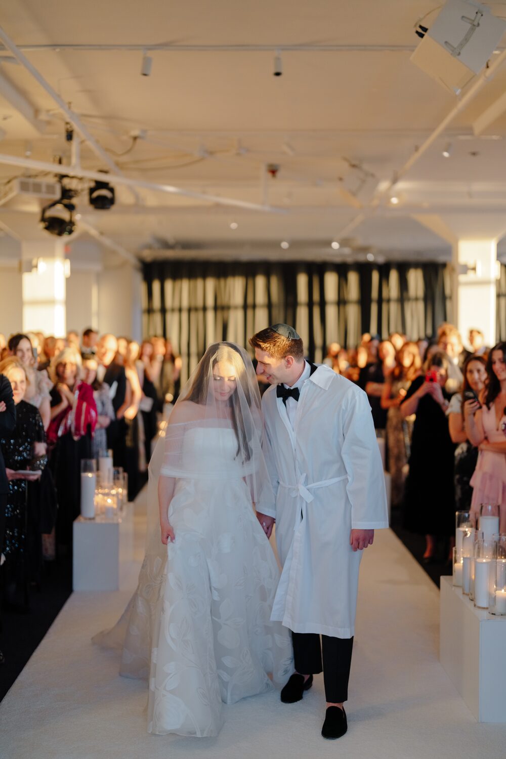 The groom in his white kittel leads the recessional through cheering guests.