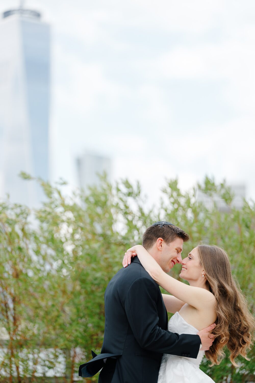 The couple holds each other among the rooftop greenery, the skyline soft behind them.
