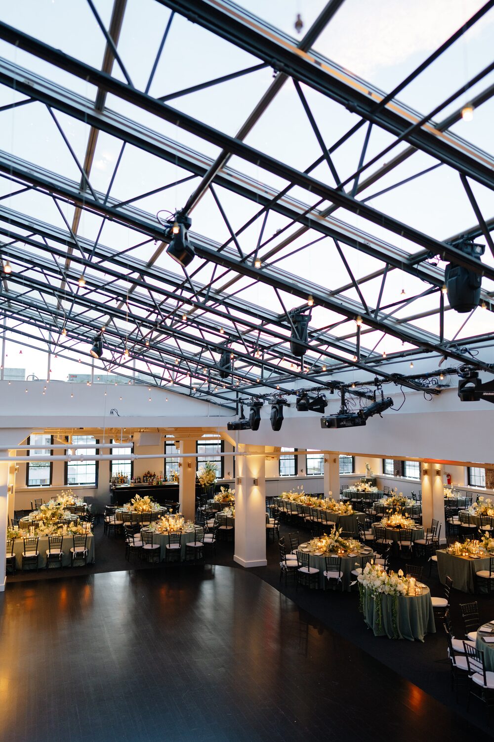 A wide view of the sage-dressed tables under the venue's steel and glass ceiling.