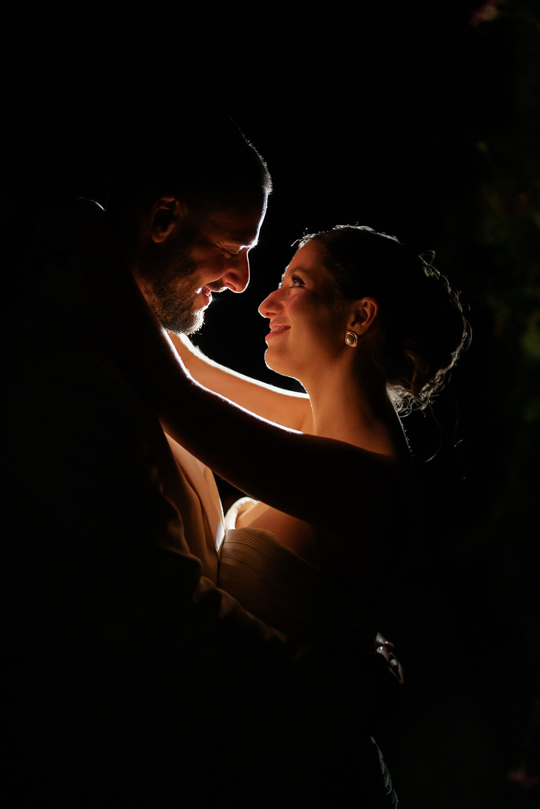 Yarden and Joel embrace at night, warm backlight tracing their faces