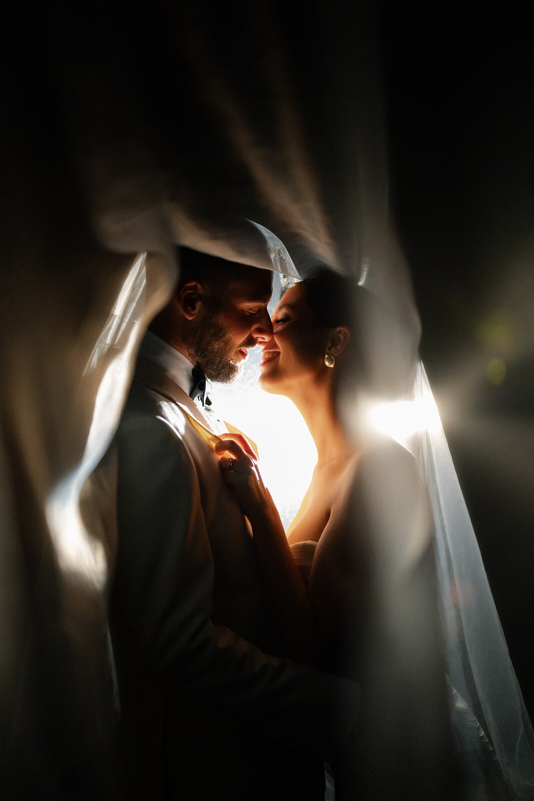 Yarden and Joel silhouetted through her veil against a single warm light