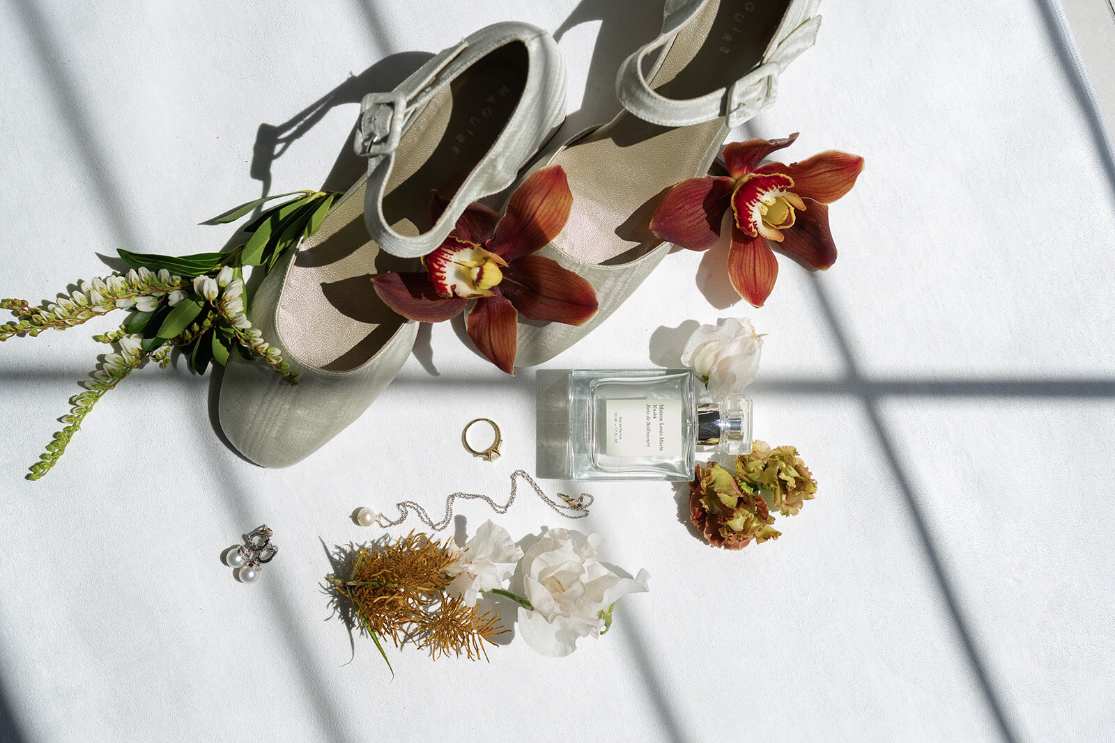 Yarden’s bridal shoes and jewelry laid out with deep red orchids and dried florals on a white table