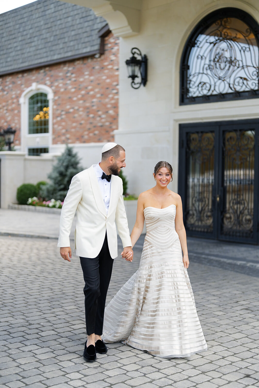 Yarden and Joel walk hand in hand across the stone courtyard in front of the estate
