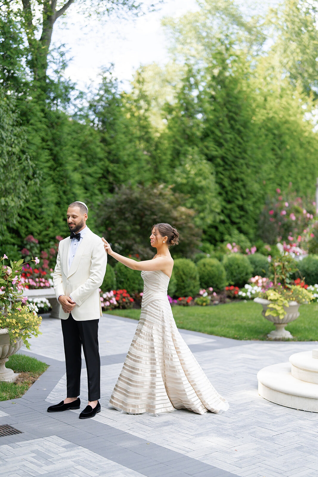 Yarden reaches Joel on the garden path for their first look, hedges and flower beds all around