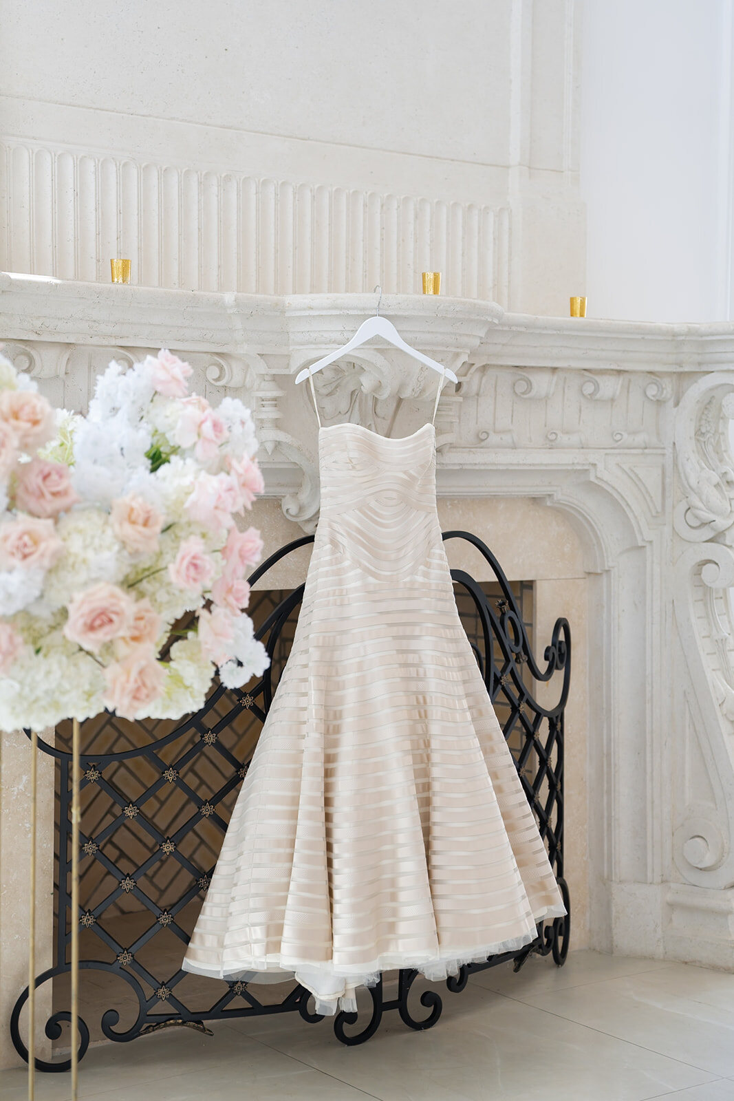 Yarden’s vintage Vera Wang gown hanging on an iron screen beside a carved marble fireplace and blush florals