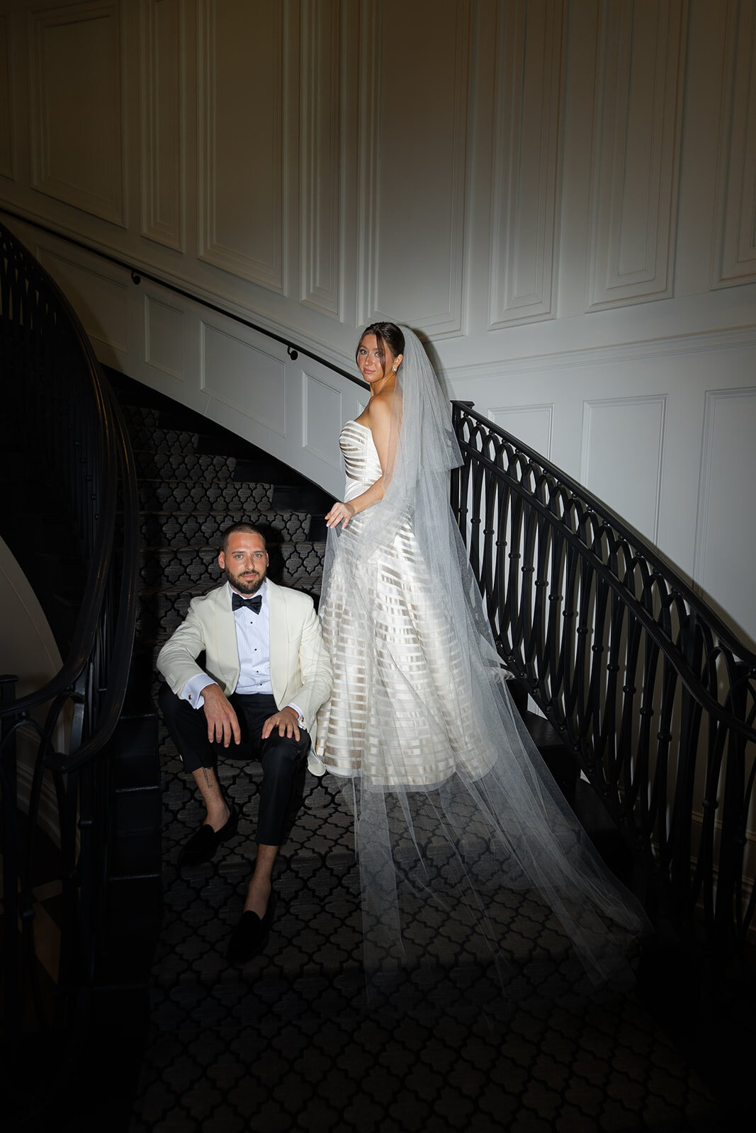 Yarden on the grand staircase with her veil trailing down the steps as Joel waits below