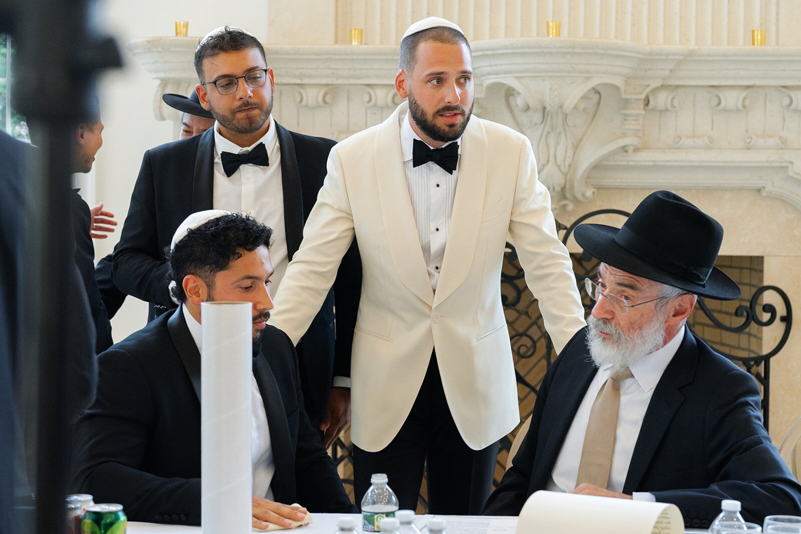Joel at the tisch in his ivory dinner jacket, surrounded by family and rabbis in black hats
