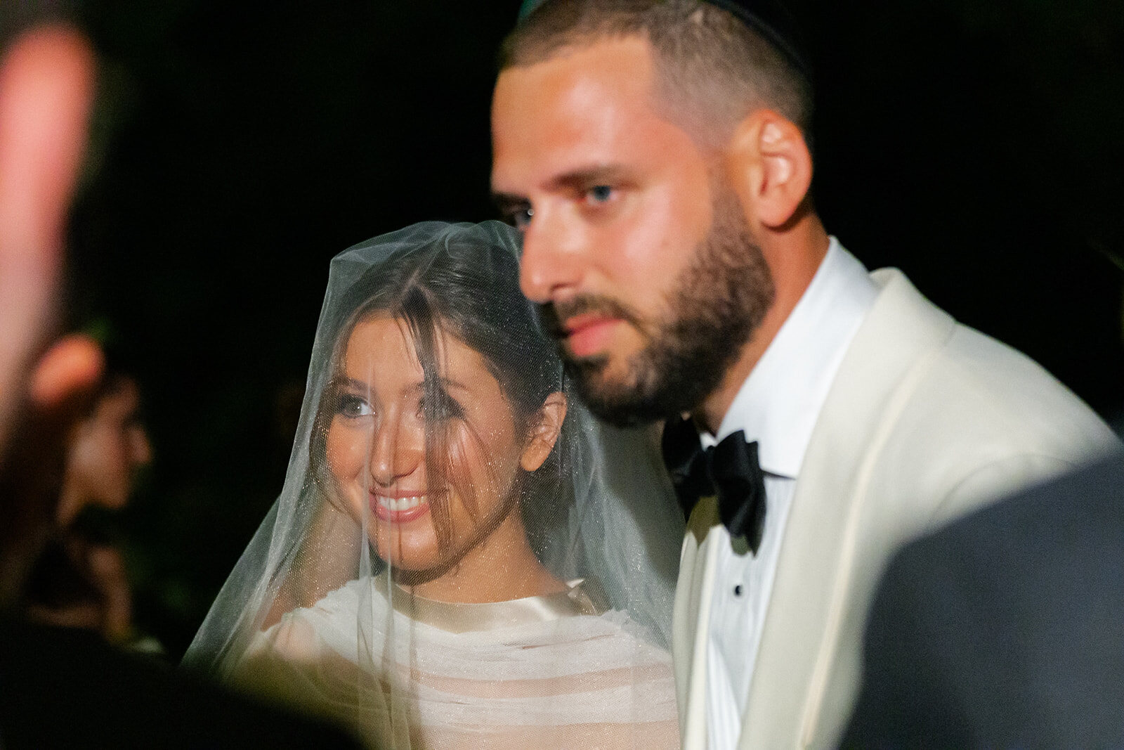 Yarden smiles beneath her veil beside Joel under the chuppah