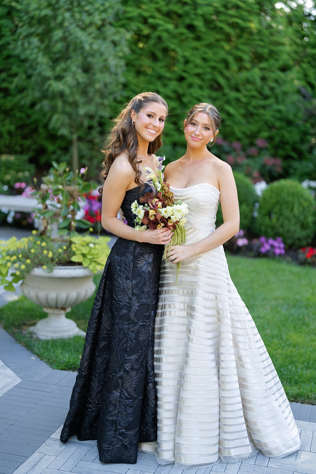 Yarden with a bridesmaid in a navy sequined gown in the gardens, holding her red and green bouquet