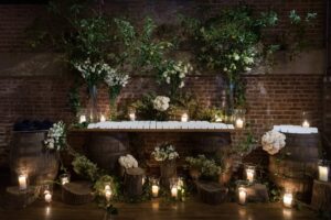 Escort card display on whiskey barrels with greenery and candlelight at the Liberty Warehouse