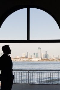 Groom silhouetted in the Liberty Warehouse arched window with the Manhattan skyline beyond