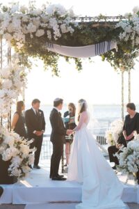 Tallit-draped chuppah with white florals at a waterfront Jewish wedding ceremony at the Liberty Warehouse