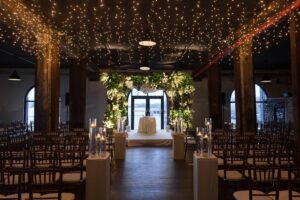 Indoor ceremony beneath twinkle lights with a greenery chuppah at the Liberty Warehouse